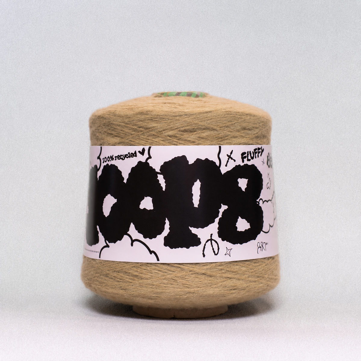 A spool of tan recycled yarn with a white paper label featuring bold black graffiti-style lettering that reads 'COPI8', set against a neutral light gray background.