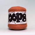 A ball of rust-orange yarn wrapped in a white paper label with bold black graffiti-style lettering, photographed against a neutral light gray background.