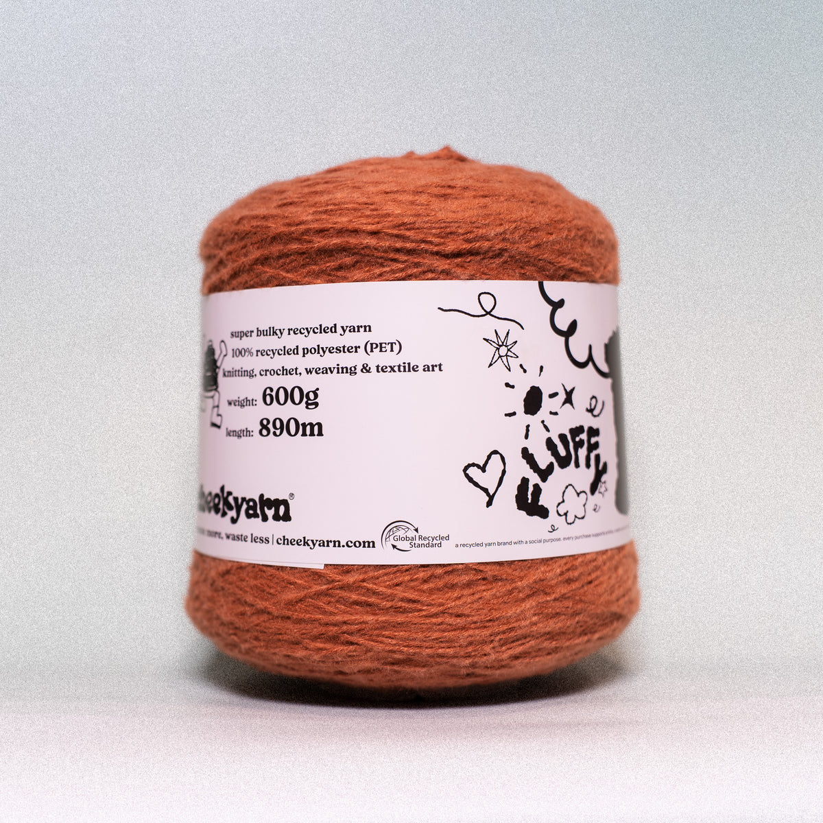 A ball of orange-brown fuzzy recycled yarn with a white paper label that reads 'cheeky yarn' and '100% recycled polyester (PET)', photographed against a light gray background.