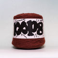 A ball of rust-brown yarn with a white paper label featuring bold black graffiti-style lettering, photographed against a neutral light gray background.